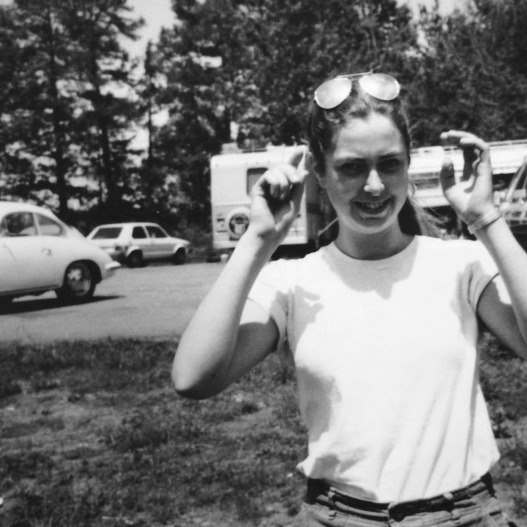 Dana with glasses, long hair, in front of vintage cars